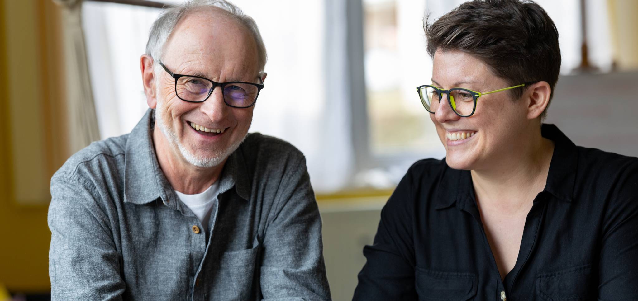 Dr. med. Cécile Barth & Dr. med. Bernhard Pirkl lächeln und sprechen gemeinsam am Tisch