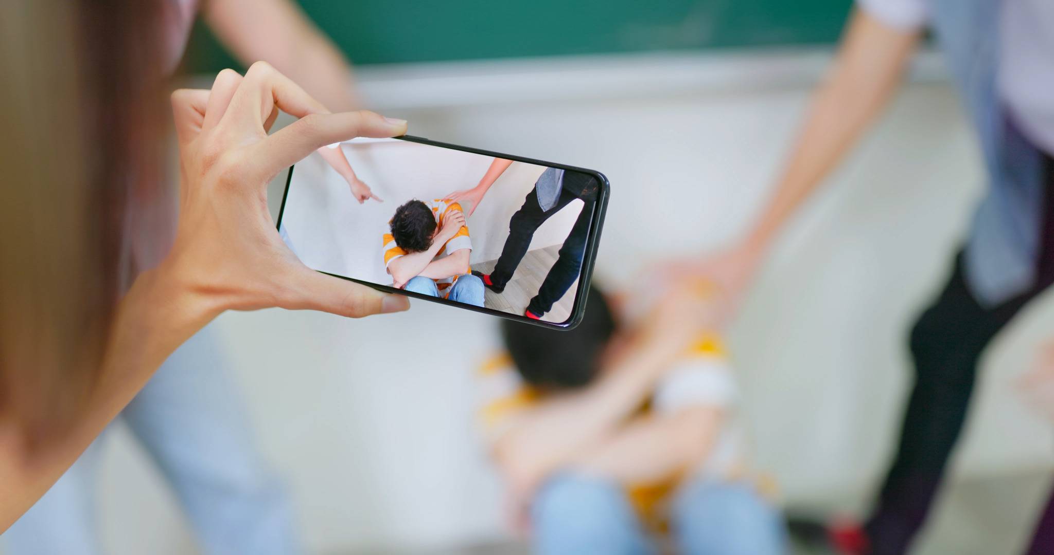 Mobbingsituation wird mit Smartphone gefilmt, Kind sitzt bedrängt am Boden.