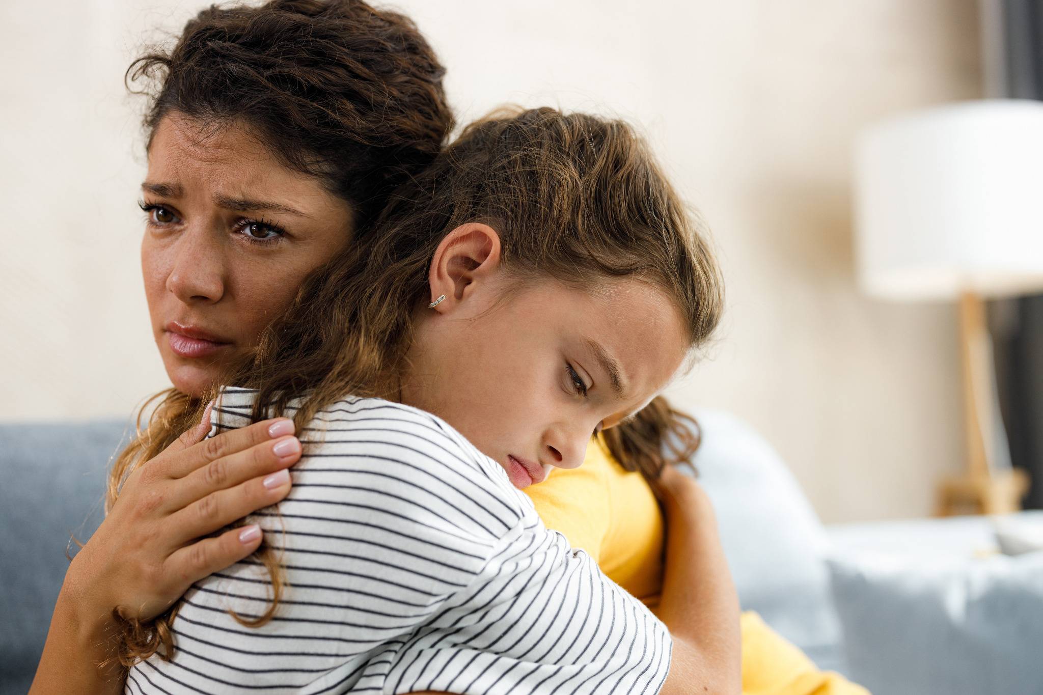 Mutter tröstet trauriges Kind und hält es schützend im Arm.