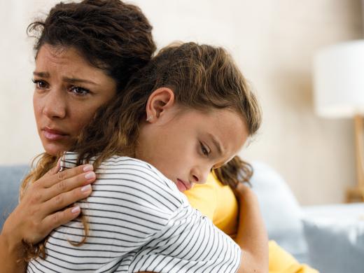 Mutter tröstet trauriges Kind und hält es schützend im Arm.